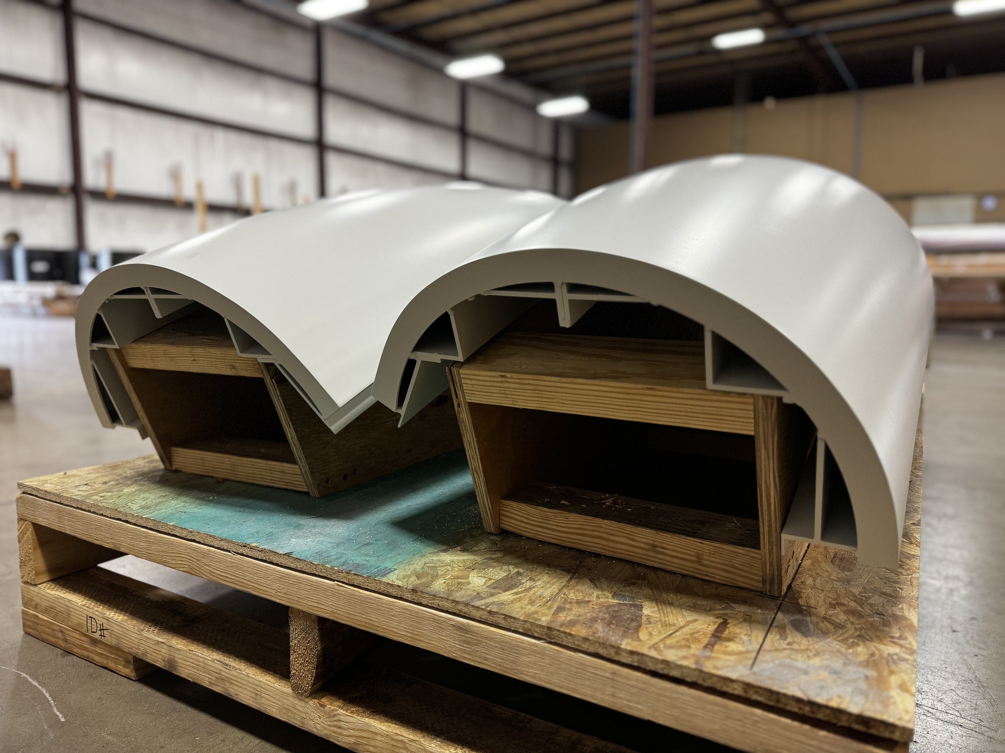 Curved painted aluminum canopy edge pieces on a pallet in the shop
