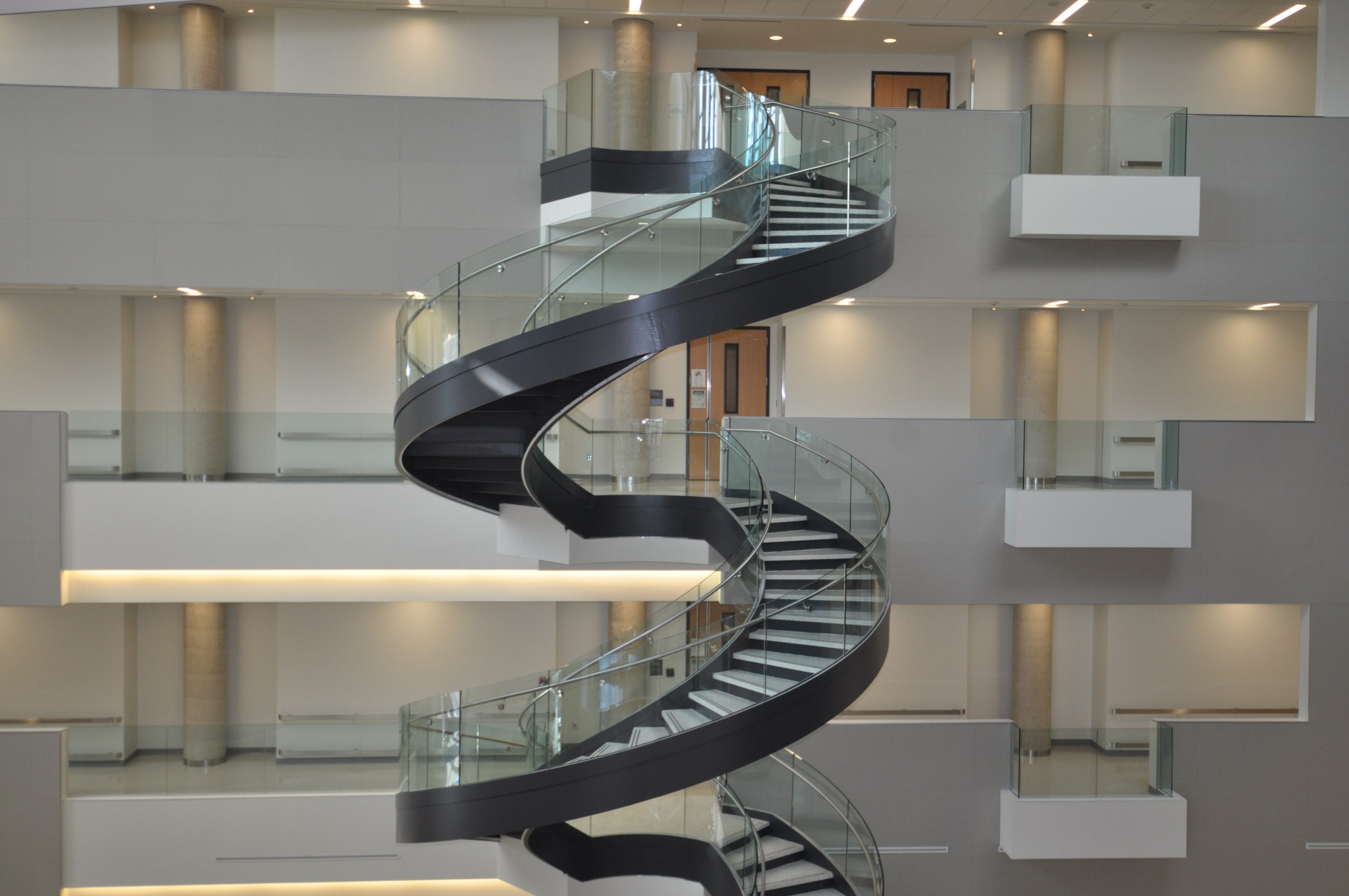 A helical staircase with glass railings climbing through three floors of a Drexel University atrium