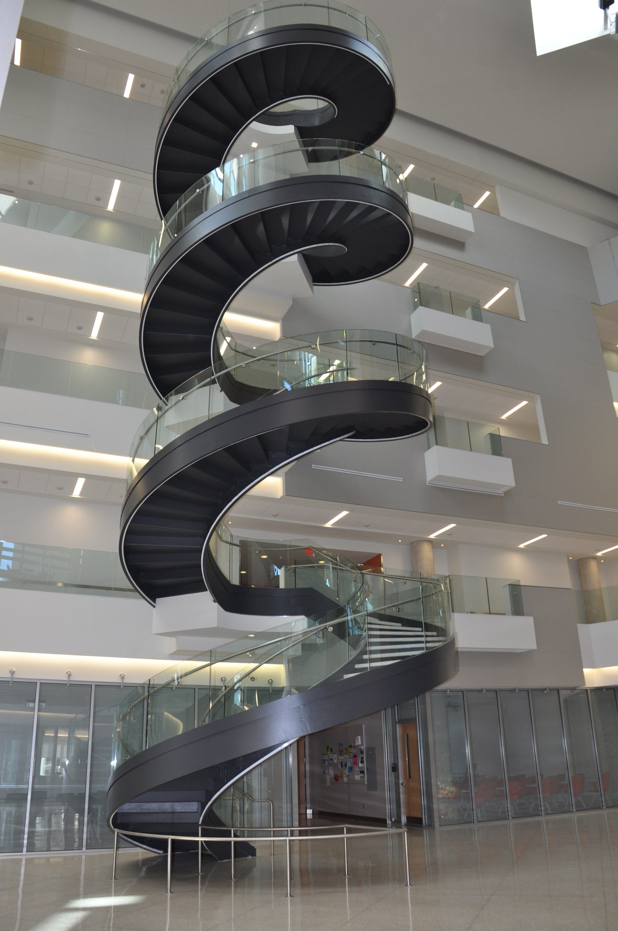 Two turns of a helical staircase with glass railings, seen across Drexel University's atrium